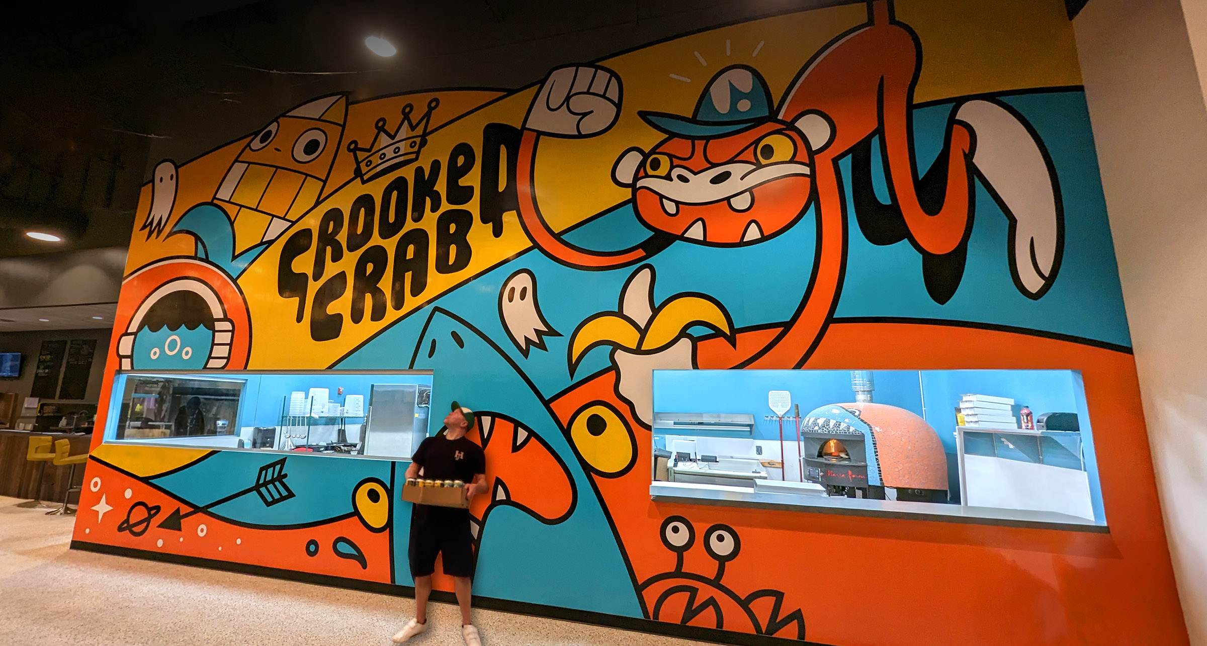 Chris standing in front of a colorful mural in the Crooked Crab taproom